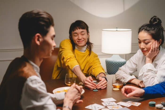 Friends playing poker at a table, smiling while collecting chips, representing the psychology and unpredictability of poker AI strategy.