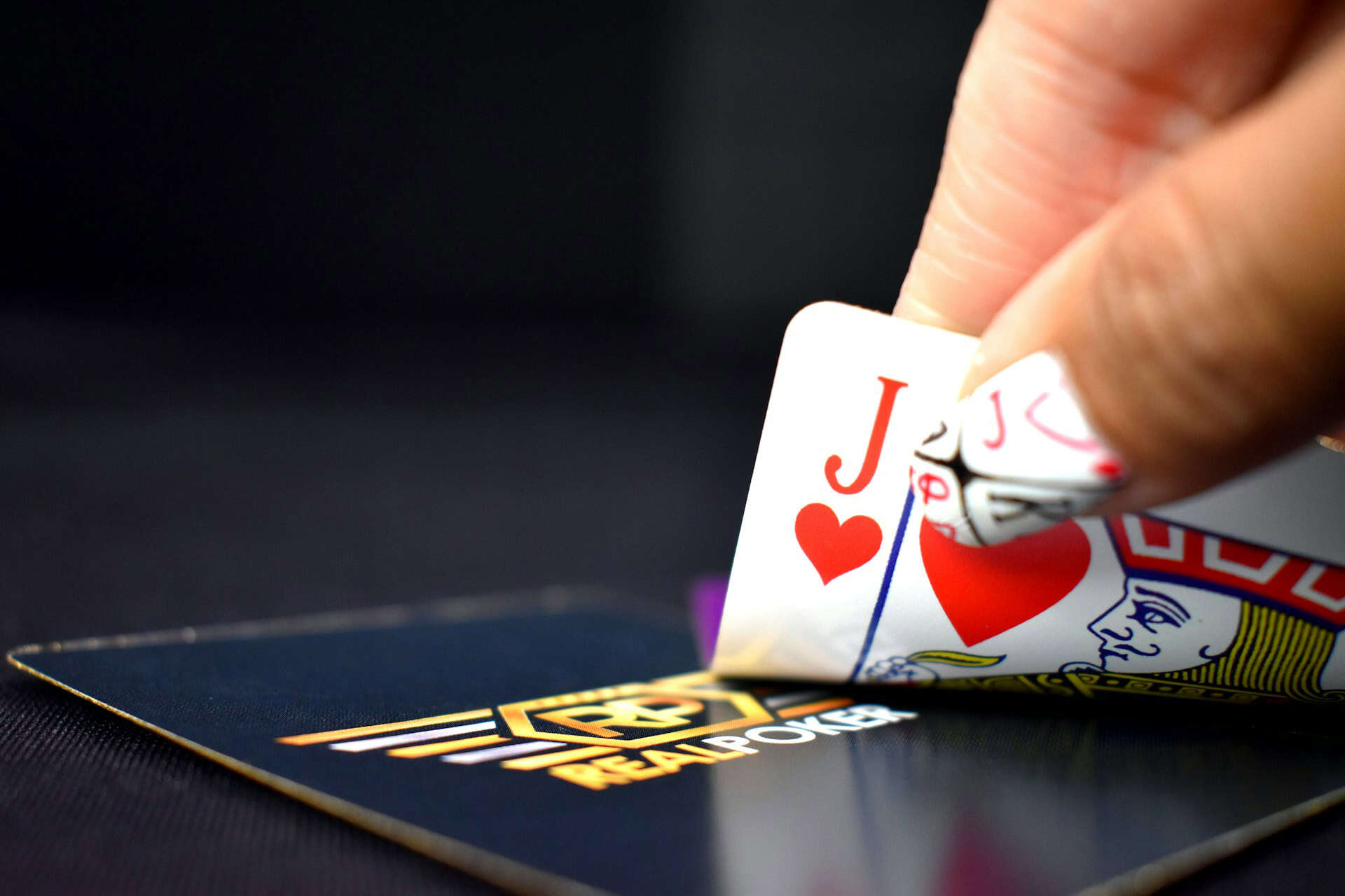 Close-up of a hand holding J of hearts over poker chips, representing LLMs in poker AI grappling with high-stakes choices.